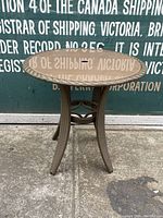 Full view of small outdoor patio table showing overall design and condition with woven style legs and central cross braces.