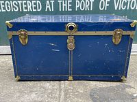 Front view of vintage blue steamer chest showing brass mounts, central lock, and two latches
