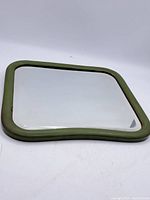 Full square mirror with green frame shown flat on white surface