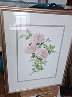 Photo of the framed watercolor painting showing pink flowers and green leaves in a gold-tone frame with matting.
