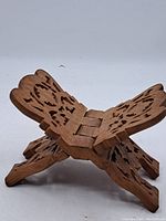 Side angle view showing foldable design and detailed hand-carved patterns on wood, with floral and decorative pierced elements.