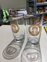 Two clear glasses with gold university insignia
