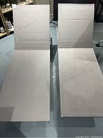 Two grey reclining chaise loungers shown upright, fabric seating and backrest with metal frame visible.