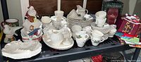 Wide shot showing full set of Christmas dinnerware including plates, cups, figurines, and decorative pieces placed on a shelf.