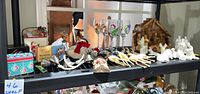 Wooden shelf displaying all the Christmas items including the wooden manger, the ceramic nativity figures, painted wine glasses, vintage reindeer, and various boxed collectibles