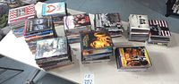 Overhead image showing multiple stacks of DVDs and CDs arranged on a table, showcasing the quantity and size of the lot.