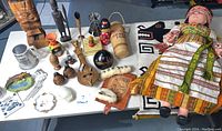 Photo showing the full collection of global souvenirs including the large Ukrainian doll, tribal wall hanging, wooden figurines, varied small souvenirs, and other items arranged on a table.