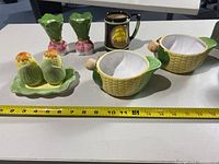 View of corn-themed ceramic kitchenware items including divided bowls, salt and pepper shakers on a tray, candle holders, small pitcher, vase, warmer with wooden handle, plus pewter beer stein, all arranged on a white surface with a measuring tape.