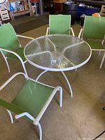Full view of white metal round outdoor table with textured glass top and four green sling chairs