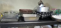 Wide shot showing stacked pie dishes, muffin pans, cake pans, baking sheets, and bag of cookie cutters and pastry bag placed on shelf.