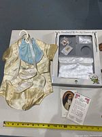 First communion baby clothing including yellow satin outfit with bonnet and booties, white ceremonial outfit set in box, and religious prayer card.