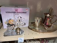 Silver-plate tea set in box with additional silver-plate pitcher and vase on shelf.