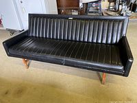 Front view of black vinyl sofa showing vertical channel tufting and wooden legs