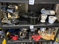 Photo of shelf with 2 stand mixers, 2 electric skillets with glass lids, crockpot insert, and 2 white ceramic vases showing arrangement and overall condition.