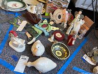 Overview of various decorative items including ceramic ducks, wooden fish, pottery bowl, wooden apples, glass pear, and angel figurines on carpet.