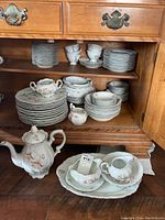 Photo of several shelves inside wood cabinet displaying multiple stacks of plates, bowls, cups, and serving pieces with floral pattern.