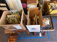 Two open boxes filled with assorted children's books sitting on small wooden tables.