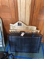 Photo showing the medium-sized foldable metal dog crate in folded state in front of a wooden door with two wooden foldable pet gates on top.