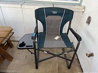 Full view of Timber Ridge folding camping chair with padded armrests, gray fabric seat and backrest, and black metal frame. Side tray with cup holder attached to the right armrest.