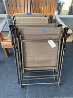 Four folded lawn chairs stacked together, showing metal frames and fabric seats, with visible wear on seats.