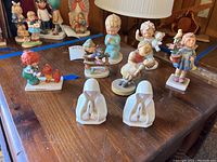 Photo showing all eight figurines on wood table, includes colorful children and two white praying figures
