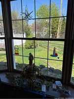 Wide view of window sill displaying the planter with statue, two stained glass sun catchers on window panes, and mini lights on table surface.