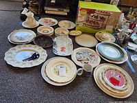Full display of assorted servingware including platters, plates, boxed Food Network 3-tier stand, pitchers, bowls, and mugs on a tabletop