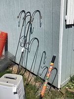 Photo of black metal shepherd hooks and flag stand leaning against blue shed on grass.
