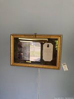 Framed Thomas Kinkade artwork titled "Sweetheart Cottage" hung on a wall, showing the gold-tone frame, integrated display light, and a caption beside the artwork.