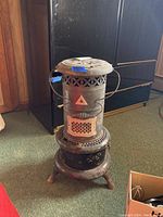 Front and side views of the vintage metal heater showing its cylindrical body, vented top, perforated panels, three legs, and control knob near the base.