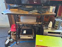 Full view of the Singer metal sewing machine base with wooden top supporting various household items under a TV setup.