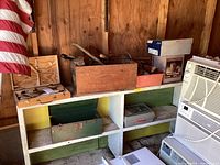 Shelving with assorted vintage metal and wooden toolboxes, some open showing tools inside. Background wooden wall and partial American flag.