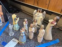 Overview photo showing nine angel figurines on carpeted floor including Willow Tree, Jim Shore, Wild Flower, and unmarked pieces.