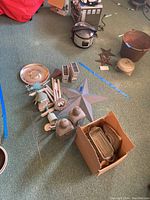 Wide view of all outdoor decorative items on green carpet including metal wind chimes, lanterns, decorative star, platter, and bucket, plus box with glass containers.