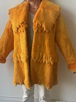 Front view of yellow sheared beaver fur coat displayed on a person wearing white pants and a gray top, showing scalloped edge design on collar, front, and hem.