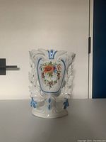 Front view of a white porcelain vase with blue accents and hand-painted red floral design on the front panel
