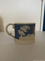 Side view showing blue and white embossed pastoral scene and handle with chip visible.
