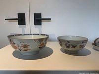 Front view of large 8″ bowl with floral and fish design on left and medium 6″ bowl with fish and floral motif on right