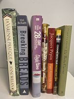Seven assorted cookbooks standing upright showing titles and authors