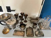 Overview of all silver plated items including teapot, bowl, goblets, flasks, pot, basket, small plate, and tray with decanters