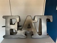 Front view photograph of the distressed metal 'EAT' wall hanging sign showing the block letters with worn silver paint and darkened edges for a vintage industrial appearance.