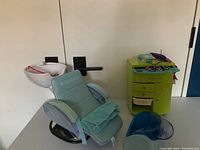 Mint green American Girl hair salon chair with attached shampoo basin, beauty parlor cart, blue hair dryers and accessories on floor