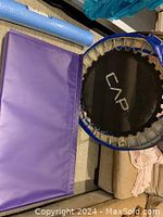 Photo showing the purple folding gymnastics mat on the floor next to the small round trampoline with blue padding and black jumping surface branded CAP.