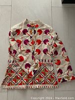 Full view of cream tunic with vibrant embroidery in purple, red, orange, and gold.