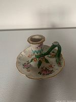 Single chamberstick showing detailed floral pattern on scalloped base, green curved handle with flowers, and gold trim on candle holder rim.