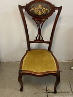 Front view of Victorian wood carved chair with upholstered yellow seat and decorative carved backrest.