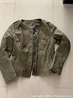 Front view of the olive green leather jacket laid flat showing button and zipper closure, slim waist, and zippered side pockets.