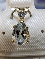 Front view close-up showing pear-shaped aquamarine and small round white gemstone in 10k gold setting on white textured jewelry display.