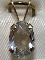 Close-up photo showing oval aquamarine gemstone in 10K gold prong setting with visible bail for chain attachment.