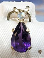 Close-up front view of the pendant showing a deep purple pear-shaped amethyst with a small round white gemstone above it, set in 10K yellow gold.